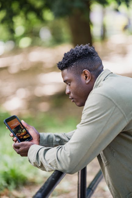 Žmogus peržiūri energijos programėlės grafiką telefone, šalia matosi namų elektros prietaisai